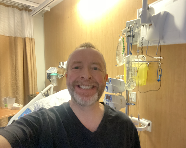 Middle aged white guy in a hospital room with equipment and curtain in background